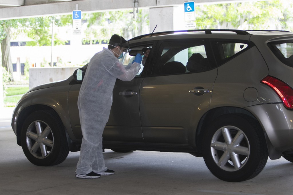 A man in a white jumpsuit and glove administers testing to a man in a car at the University of Central Florida parking garage.