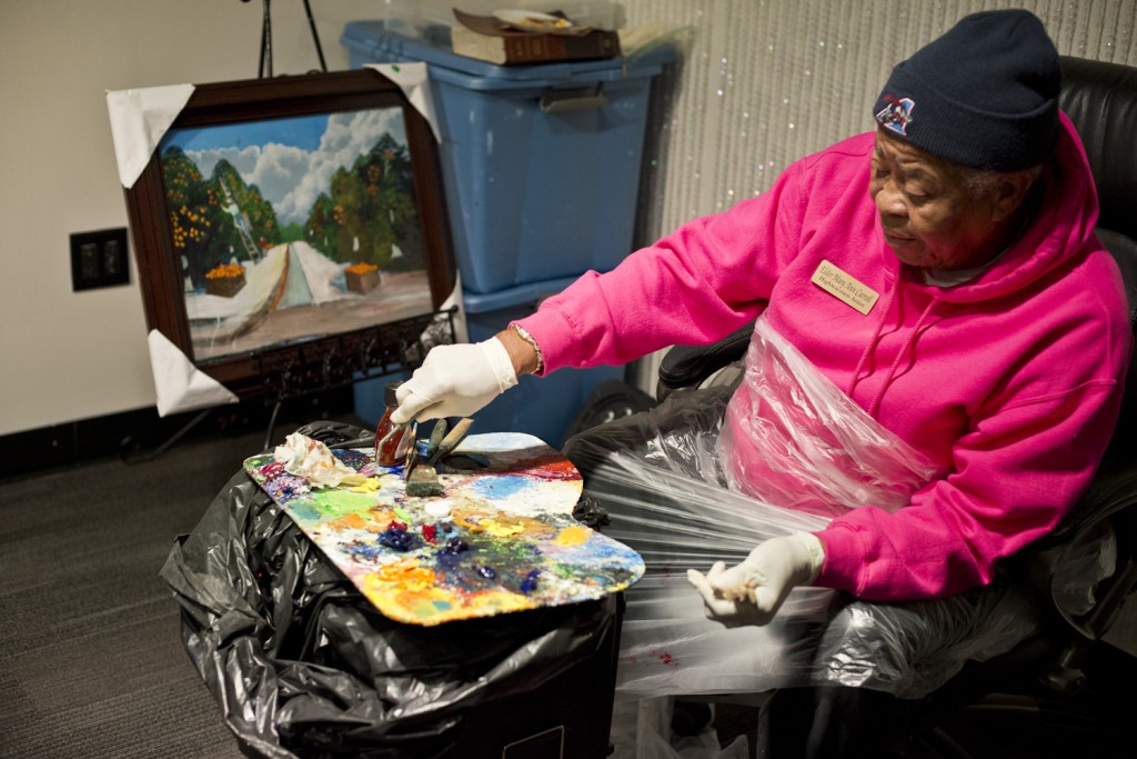 Mary Ann Carroll unpick sweatshirt with palette on her lap and painting on easel. 