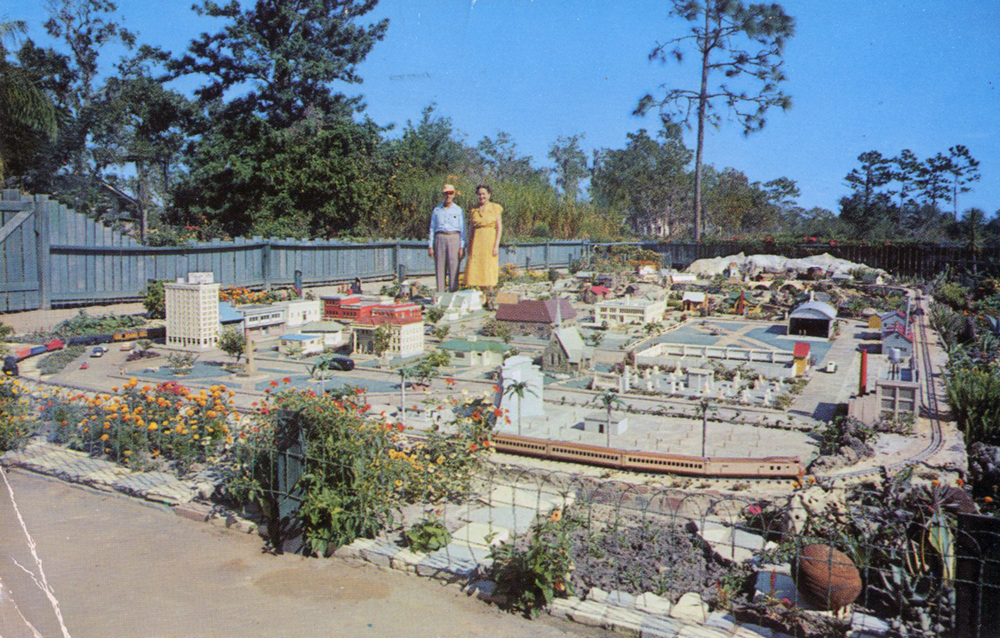 Vintage postcard shows couple standing in model of a town.