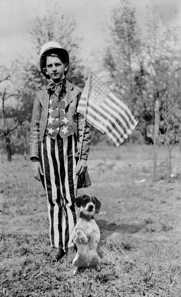 Black and white photo of young man in Uncle San outfit holding an American flag. At his feet is photoshopped dog.