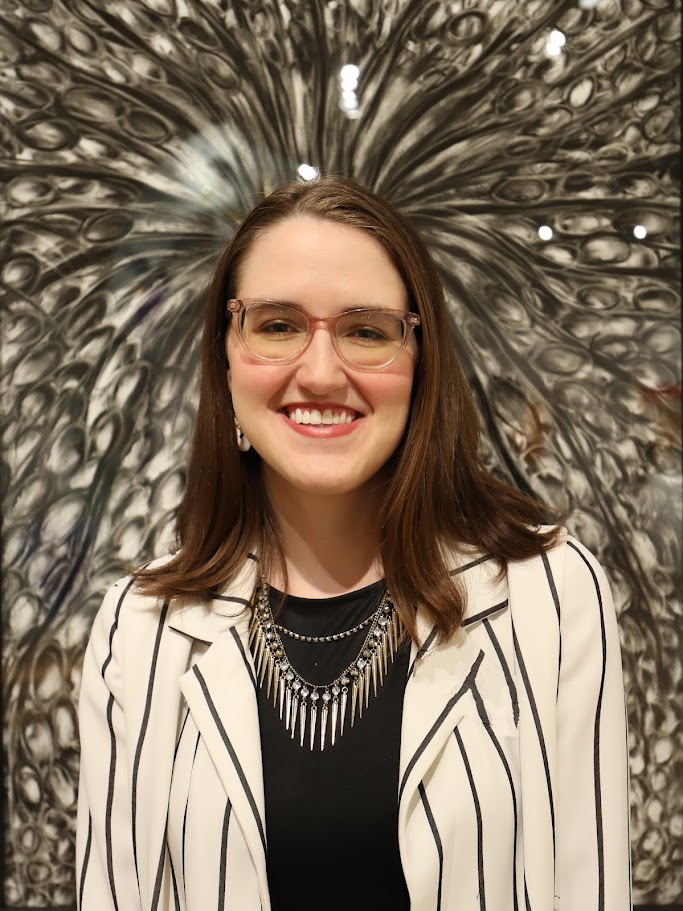 Headshot image of Kallie Turner. She is wearing a white and black blazer with a black shirt and silver tiered necklace. The background is a black and white abstract pattern